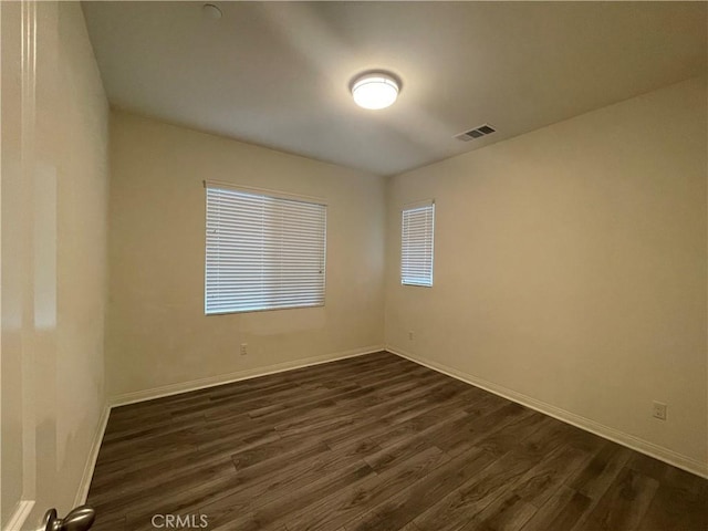 spare room with baseboards, visible vents, and dark wood finished floors