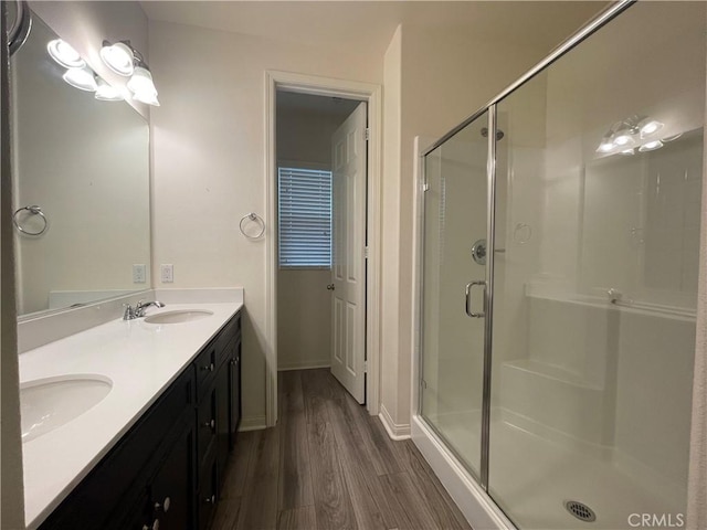 bathroom featuring double vanity, a shower stall, a sink, and wood finished floors