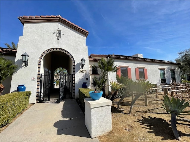 entrance to property with a tiled roof, a gate, and stucco siding