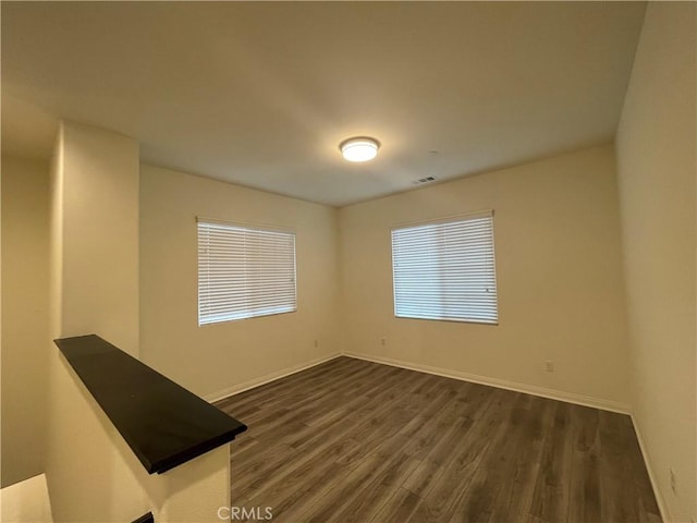 spare room with visible vents, baseboards, and dark wood finished floors