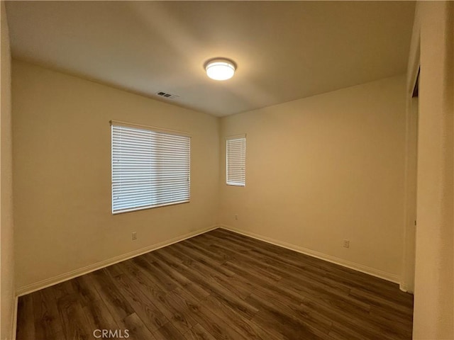 spare room featuring dark wood-style flooring, visible vents, and baseboards