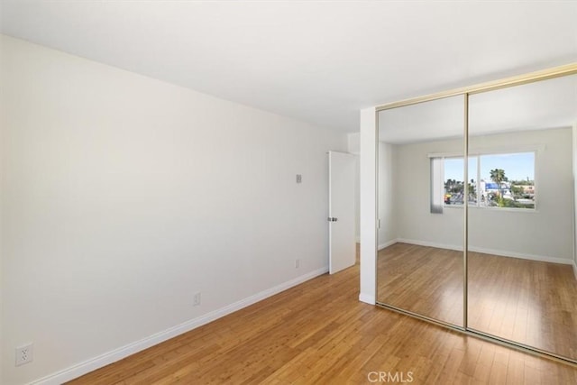 unfurnished bedroom featuring baseboards, light wood-style flooring, and a closet