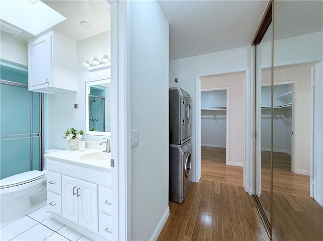 bathroom featuring vanity, toilet, stacked washer / dryer, wood finished floors, and a spacious closet