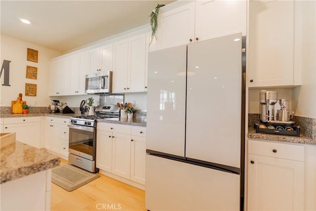 kitchen featuring stainless steel appliances, white cabinets, light wood finished floors, and light stone counters