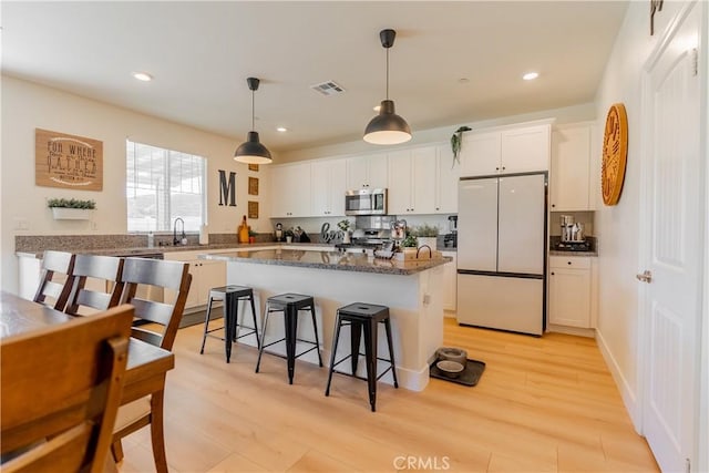 kitchen featuring a center island, a breakfast bar, light wood-style flooring, appliances with stainless steel finishes, and white cabinetry