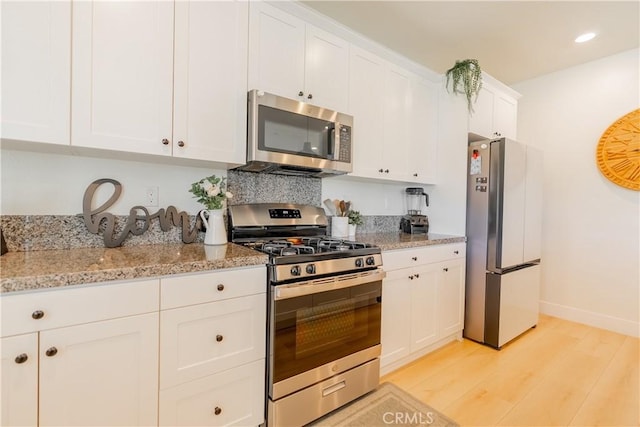 kitchen featuring recessed lighting, stainless steel appliances, white cabinetry, light stone countertops, and light wood finished floors