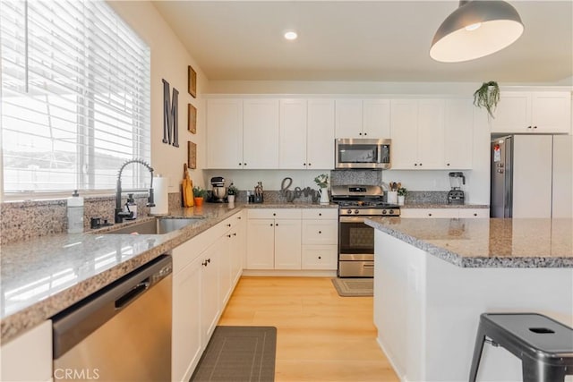 kitchen featuring light stone countertops, white cabinetry, stainless steel appliances, and a sink