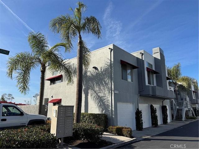 view of side of property with an attached garage, mail area, and stucco siding