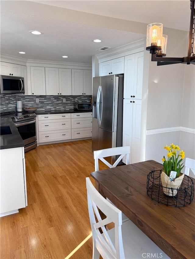 kitchen featuring stainless steel appliances, light wood-style floors, dark countertops, and white cabinets