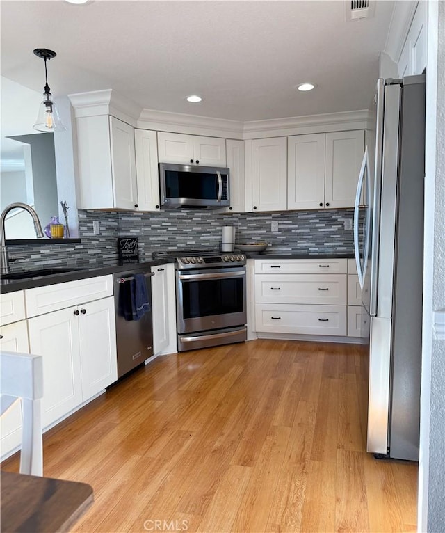 kitchen with stainless steel appliances, white cabinetry, light wood-type flooring, dark countertops, and decorative light fixtures