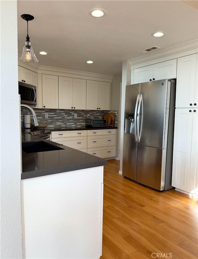 kitchen with light wood finished floors, stainless steel appliances, dark countertops, visible vents, and white cabinets