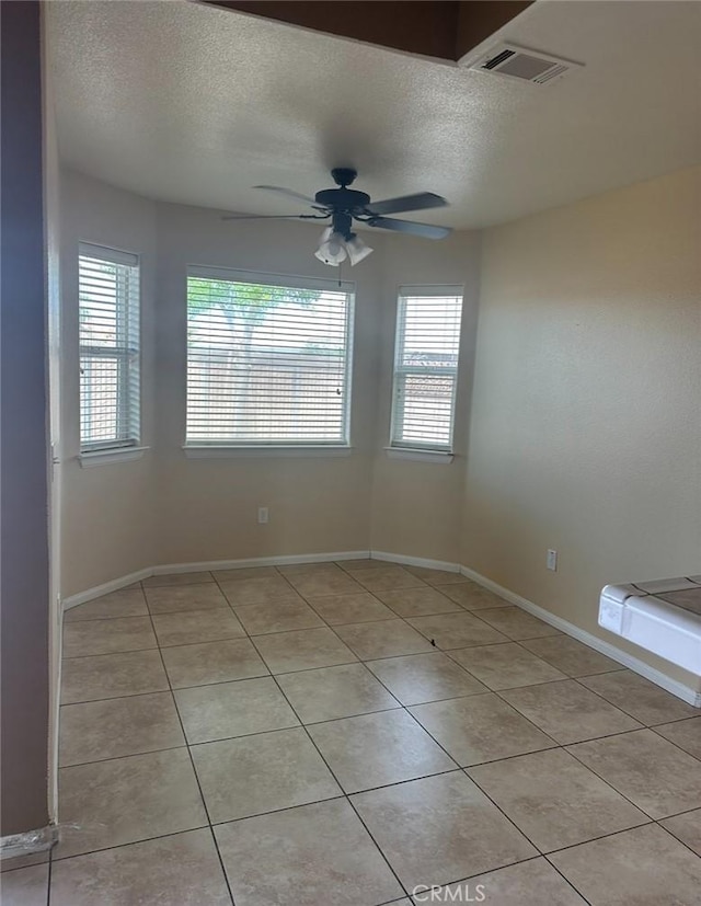 empty room with light tile patterned floors, a textured ceiling, visible vents, and a ceiling fan