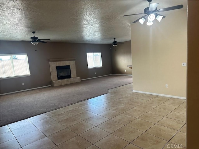 unfurnished living room featuring light tile patterned floors, a textured ceiling, a tile fireplace, light carpet, and a ceiling fan