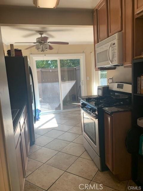 kitchen with ceiling fan, stainless steel appliances, ornamental molding, and light tile patterned floors