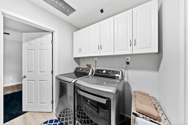 clothes washing area with separate washer and dryer, light hardwood / wood-style flooring, and cabinets