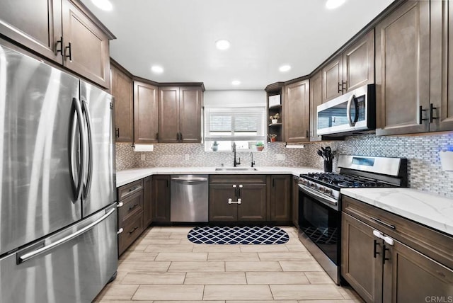 kitchen featuring sink, light stone counters, dark brown cabinets, appliances with stainless steel finishes, and backsplash