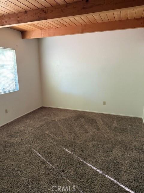 carpeted empty room with beamed ceiling and wooden ceiling