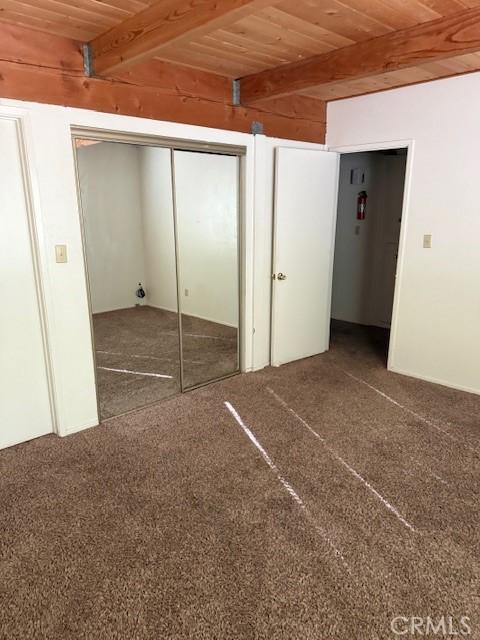 unfurnished bedroom featuring beamed ceiling, carpet floors, wood ceiling, and a closet