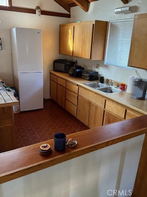 kitchen featuring white refrigerator, sink, and vaulted ceiling with beams