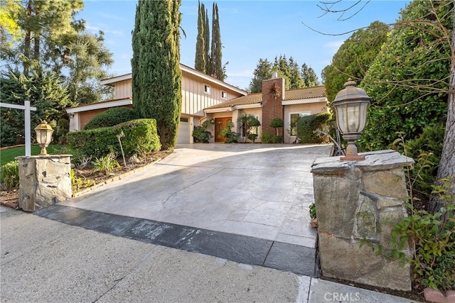 view of front of home with a tile roof, an attached garage, driveway, and a chimney