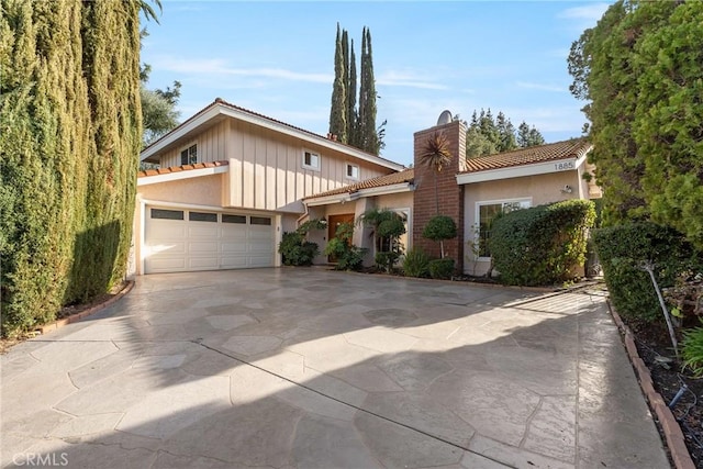 mid-century home featuring board and batten siding, concrete driveway, stucco siding, a chimney, and an attached garage