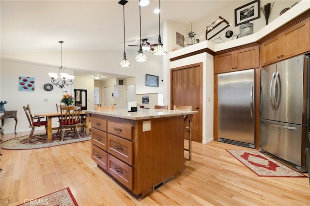 kitchen featuring pendant lighting, stainless steel refrigerator, built in refrigerator, a center island, and light stone counters