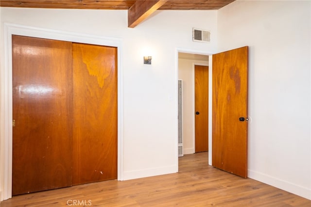 unfurnished bedroom featuring lofted ceiling with beams, a closet, and light wood-type flooring