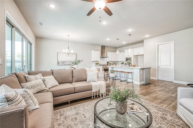 living room featuring ceiling fan with notable chandelier and light hardwood / wood-style flooring