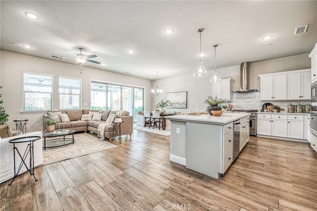 kitchen featuring pendant lighting, wall chimney range hood, appliances with stainless steel finishes, white cabinetry, and a center island