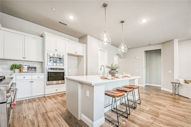 kitchen with a kitchen island with sink, hanging light fixtures, white cabinets, and appliances with stainless steel finishes