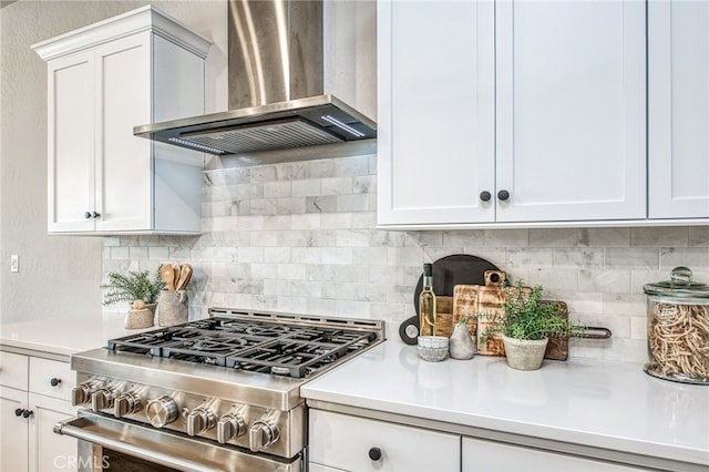 kitchen featuring wall chimney range hood, decorative backsplash, gas stove, and white cabinets