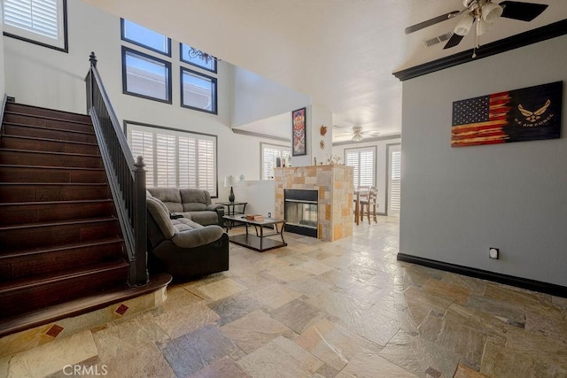 living room featuring a tiled fireplace, ceiling fan, and a high ceiling