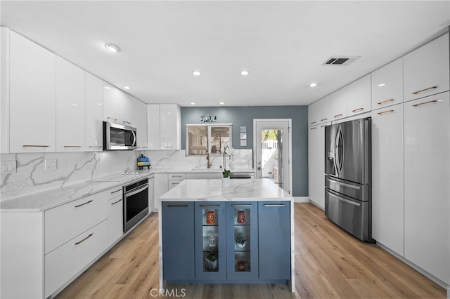 kitchen featuring stainless steel appliances, tasteful backsplash, light stone counters, white cabinets, and a kitchen island