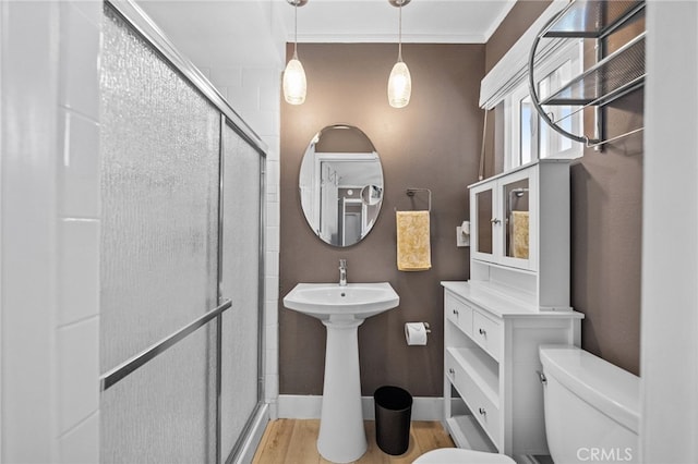 bathroom featuring ornamental molding, wood-type flooring, toilet, and a shower with shower door