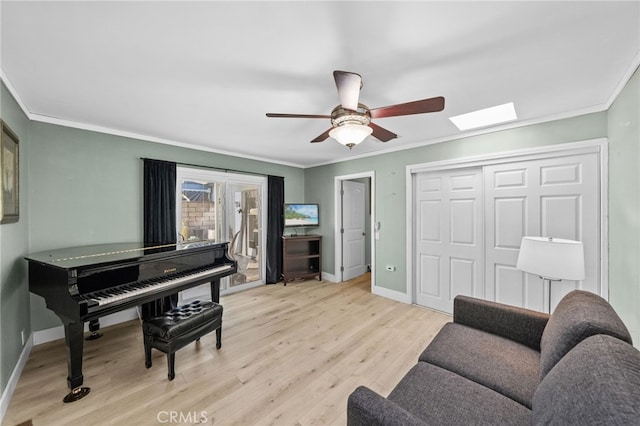 sitting room with ornamental molding, ceiling fan, light wood-type flooring, and a skylight