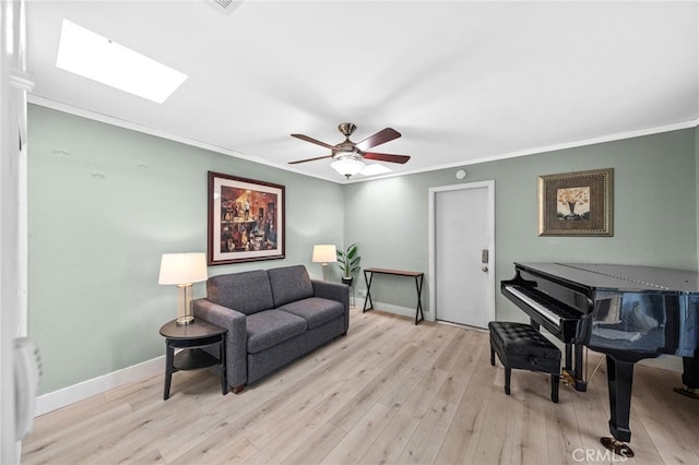 living area with crown molding, ceiling fan, a skylight, and light hardwood / wood-style floors