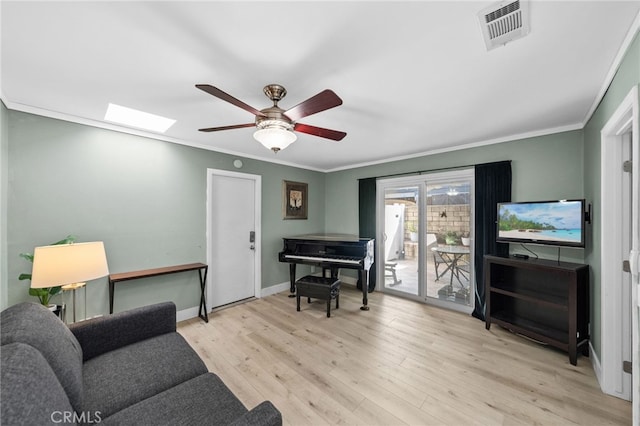 living room featuring ceiling fan, ornamental molding, a skylight, and light wood-type flooring