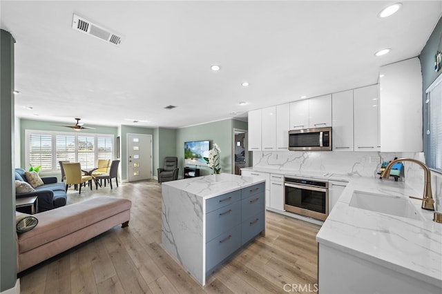 kitchen featuring sink, stainless steel appliances, light stone counters, white cabinets, and decorative backsplash