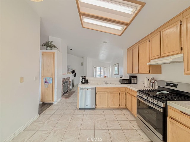 kitchen featuring vaulted ceiling, stainless steel appliances, light brown cabinetry, and tile counters