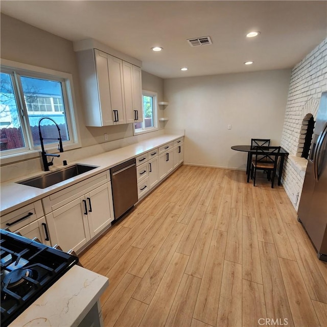 kitchen featuring appliances with stainless steel finishes, sink, light hardwood / wood-style flooring, and white cabinets