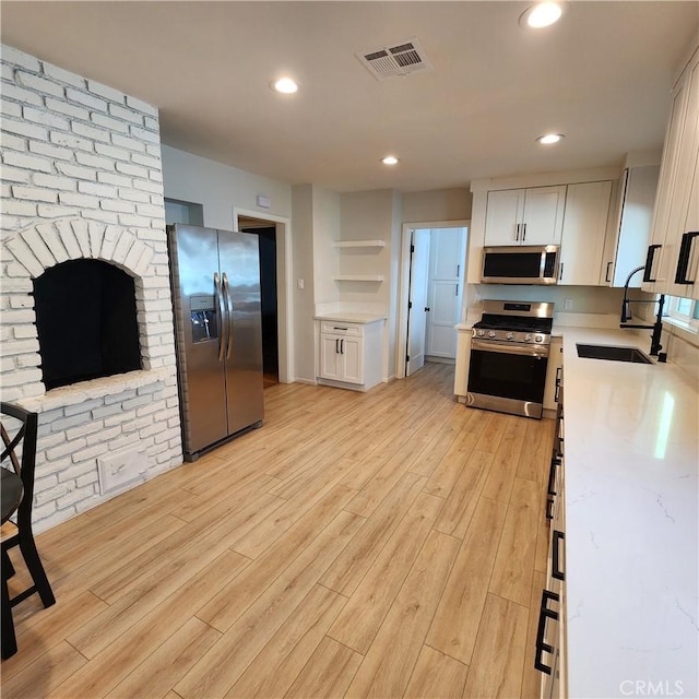 kitchen with appliances with stainless steel finishes, sink, white cabinets, light stone counters, and light hardwood / wood-style floors