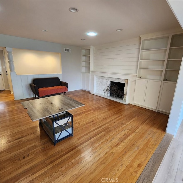 living room featuring built in shelves, a fireplace, and light hardwood / wood-style floors