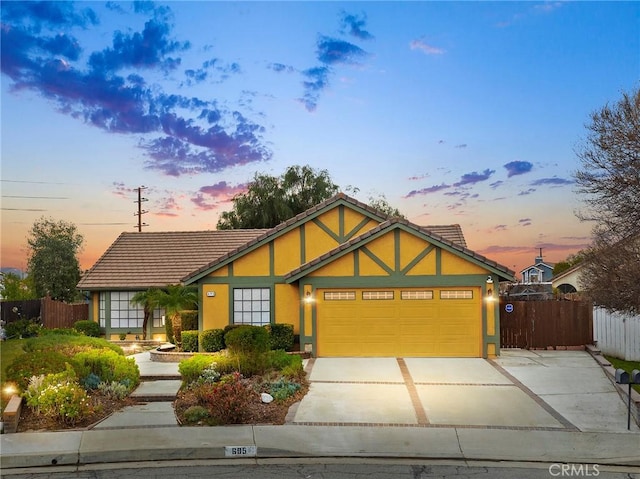 view of front of home featuring an attached garage, fence, a tile roof, concrete driveway, and stucco siding