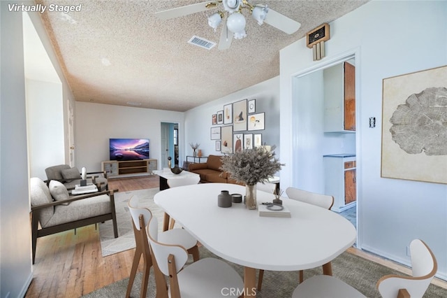 dining area featuring ceiling fan, wood-type flooring, and a textured ceiling