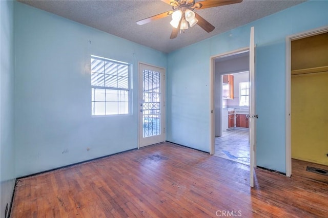 unfurnished room with ceiling fan, plenty of natural light, wood-type flooring, and a textured ceiling