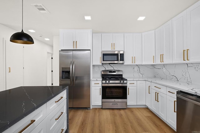 kitchen featuring stainless steel appliances, dark stone countertops, white cabinets, and decorative light fixtures