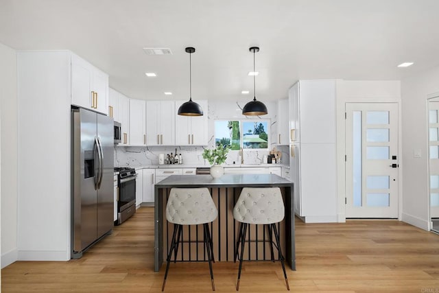 kitchen with a center island, light hardwood / wood-style flooring, pendant lighting, stainless steel appliances, and white cabinets