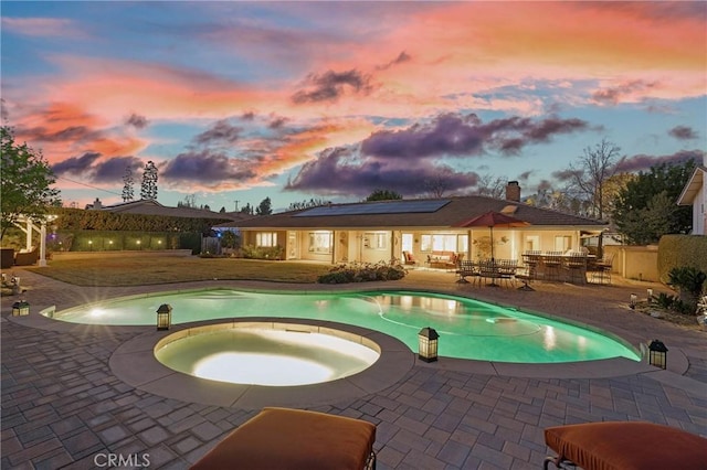 pool at dusk featuring a patio and an in ground hot tub