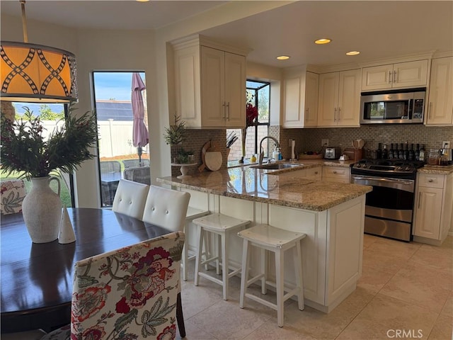 kitchen with appliances with stainless steel finishes, a peninsula, light stone countertops, hanging light fixtures, and a sink