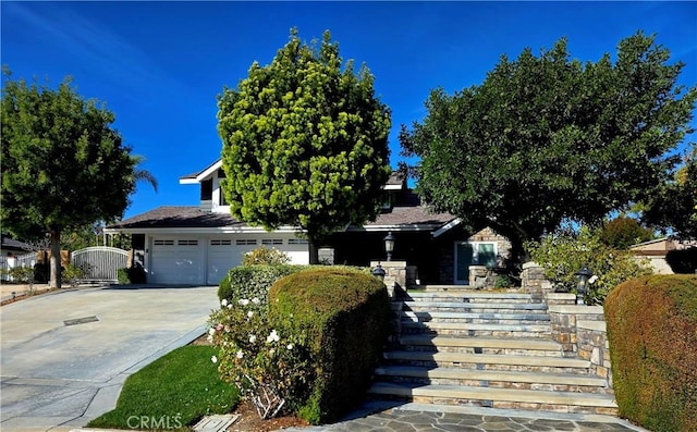 view of property hidden behind natural elements featuring concrete driveway and an attached garage